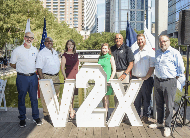 Speakers from the kickoff event pose next to the V2X sign. From left to right: TxDOT’s Marc Williams, TTI’s Greg Winfree, Texas A&M Transportation Services’ Debbie Lollar, Congresswoman Lizzie Fletcher, FHWA’s Shailen Bhatt, Intelligent Transportation Society of America’s Bobby McCurdy and Audi of America’s Brad Stertz.